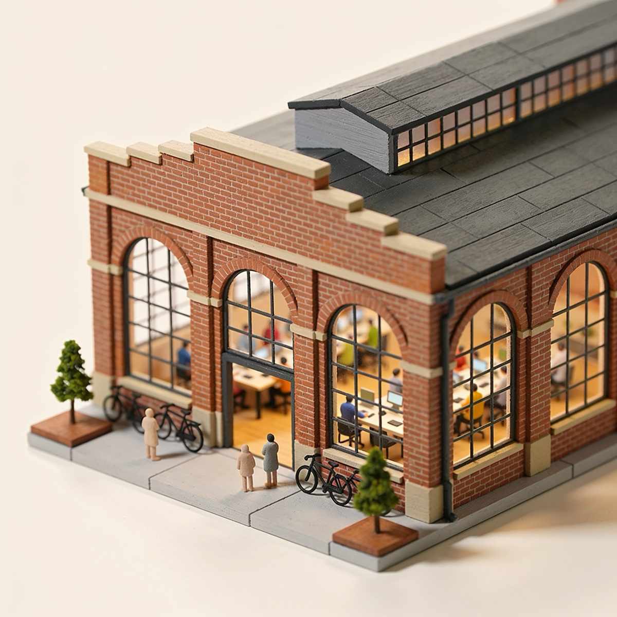A miniature brick warehouse with tall arched windows and people at long tables inside, bikes parked outside